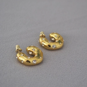 Macro detail of thick gold-plated C-shaped earrings with sparkling cubic zirconia inlay