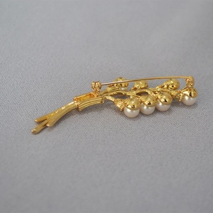Macro shot of gold floral brooch featuring white pearls and textured branch detail