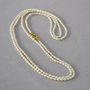Détail de perles d'eau douce en forme de riz avec fermoir OT doré sur fond texturé gris