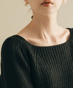 Dettaglio di una sottile collana a catena serpente d'argento con maglione nero a maglia