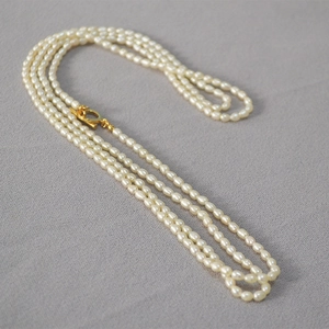 Collier long élégant en perles de riz blanches avec fermoir OT doré sur tissu gris