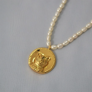 Close-up of a gold cat head coin pendant on a freshwater pearl choker necklace