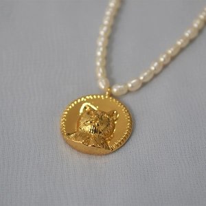 Macro detail of golden cat head relief pendant with white freshwater pearls necklace