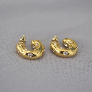 Chunky gold-plated C-shaped earrings with sparkling crystals on grey fabric