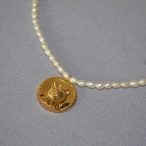 Vintage freshwater pearl necklace featuring a gold embossed cat coin pendant on gray fabric