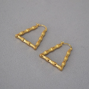 Macro shot of gold-plated triangle bamboo-textured earrings on grey fabric surface