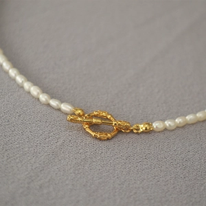 Élégant collier de perles avec fermoir OT doré sur fond gris de style minimaliste