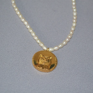 Macro shot of freshwater pearl necklace with detailed gold cat head coin pendant