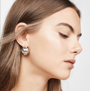 Close-up of a large polished silver hollow ball earring worn by a model in a minimalist style