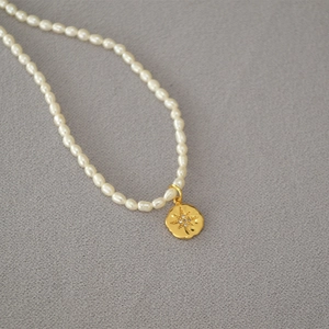 Detailed view of rice-shaped freshwater pearls with a star engraved gold coin pendant