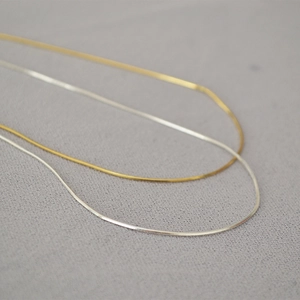 Collana a catena a serpente ultrasottile minimalista in oro e argento su fondo grigio