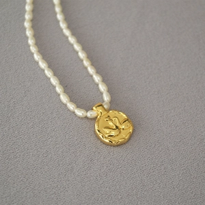 Close-up of freshwater pearl necklace featuring a vintage embossed gold coin pendant