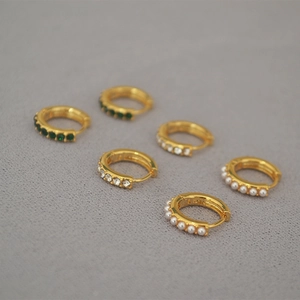 Detailed view of three pairs of gold-plated hoop earrings with green stones and pearls
