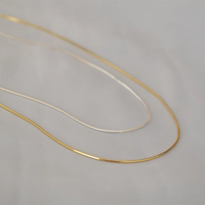 Dettaglio di collane minimaliste in oro e argento su tessuto grigio testurizzato