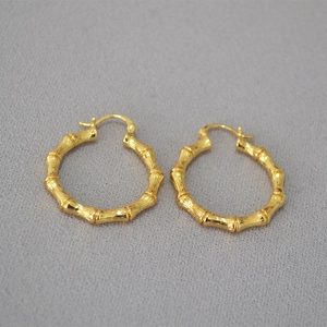 Macro shot of gold-plated hoop earrings featuring a detailed bamboo texture design