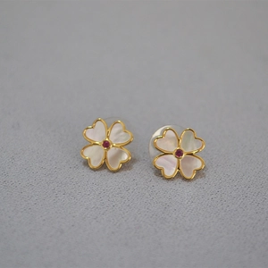 Vue macro des boucles trèfles avec nacre blanche et pierre précieuse rouge centrale