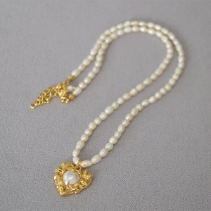 Detail of vintage gold heart pendant on a freshwater seed pearl necklace with lobster clasp