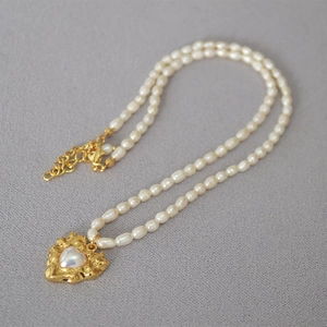 Detailed close-up of a heart-shaped gold pendant with irregular pearl and tiny rice pearls