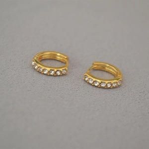 Detail of gold-plated hoop earrings with small white zircons on a grey fabric background