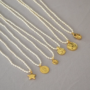 Macro shot of six freshwater rice pearl necklaces with assorted gold vintage coin pendants