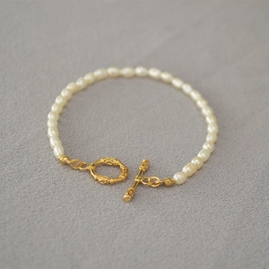 Détail du fermoir OT doré et des perles blanches sur un bracelet élégant