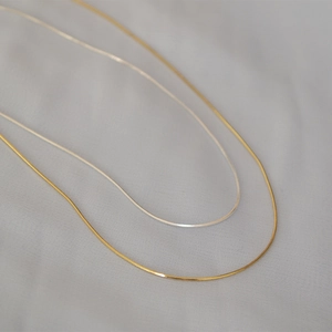 Vista macro della catena a serpente ultra sottile oro e argento su tessuto grigio