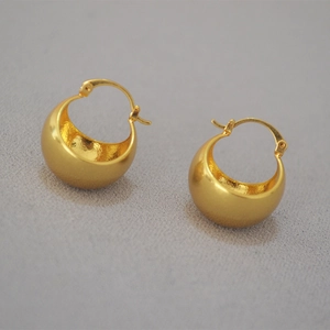 Detail of chunky gold-plated teardrop hoop earrings on grey textured fabric background