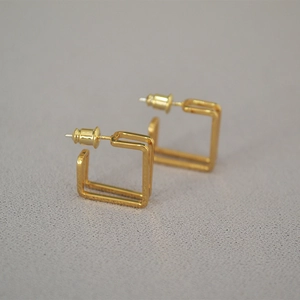Macro shot of minimalist gold plated square hoop earrings with a double line metal design