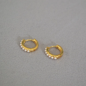 Close-up of gold plated hoop earrings with six white pearls on textured grey fabric