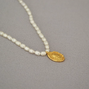 Vintage French pearl necklace with a gold coin queen pendant on textured gray fabric