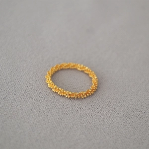 Macro shot of minimalist gold braided chain ring with fine woven texture and shiny finish