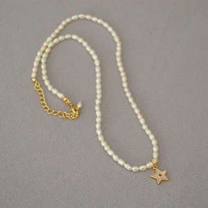 Detail of freshwater pearl necklace with gold star pendant and red zircon stone