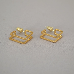 Minimalist double hollow square gold plated stud earrings on grey fabric background