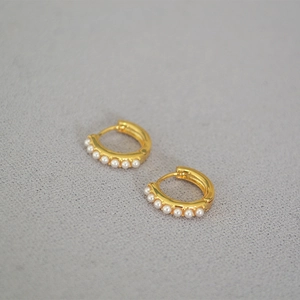 Macro view of gold hoop earrings featuring small white pearls in a minimalist design