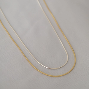 Dettaglio di collane a catena serpente minimaliste in oro e argento su tessuto testurizzato