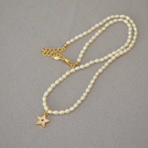 Freshwater pearl necklace featuring a gold star pendant with red gemstone on grey fabric