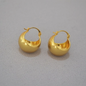 Macro detail of chunky gold-plated brass hoop earrings on a textured fabric background
