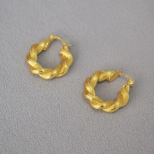 Macro detail of 18K gold-plated twisted rope hoop earrings on gray fabric