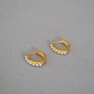 Detailed macro view of gold-plated hoop earrings with small white pearls on textured surface