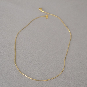 Dettaglio macro della collana a catena serpente placcata oro su tessuto grigio testurizzato