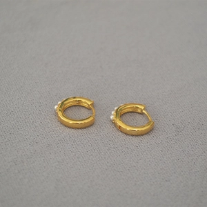 Macro view of gold hoop earrings with small pearls on a textured grey background