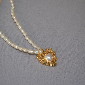 Macro detail of irregular gold heart pendant set with white pearl on a pearl chain