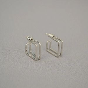 Macro view of geometric double hollow rectangular 925 silver stud earrings on grey fabric