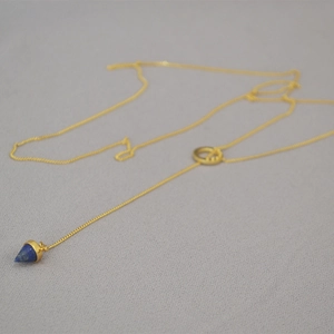 Detail of gold Y-chain necklace featuring a blue lapis lazuli cone pendant on grey texture
