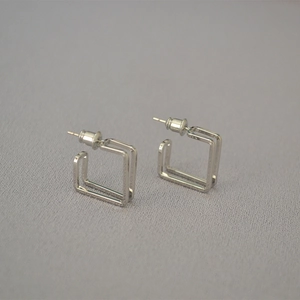 Detail shot of silver square double-layer earrings on grey textured fabric background