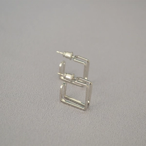 Detail view of square double-layered silver stud earrings with parallel metal lines