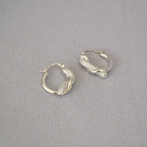 Dettaglio di orecchini a cerchio a nodo d'argento con pavé di pietre di zirconia cubica