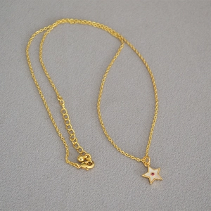 Detailed shot of a gold star pendant necklace with pink gemstone on a grey textured fabric