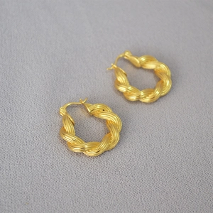 Macro detail of golden twisted hoop earrings featuring intricate woven texture design