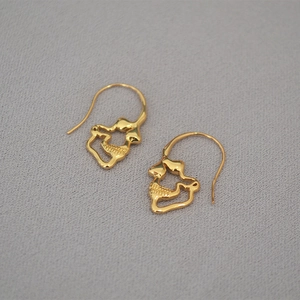 Macro detail of gold-plated skull drop earrings with intricate hollow design